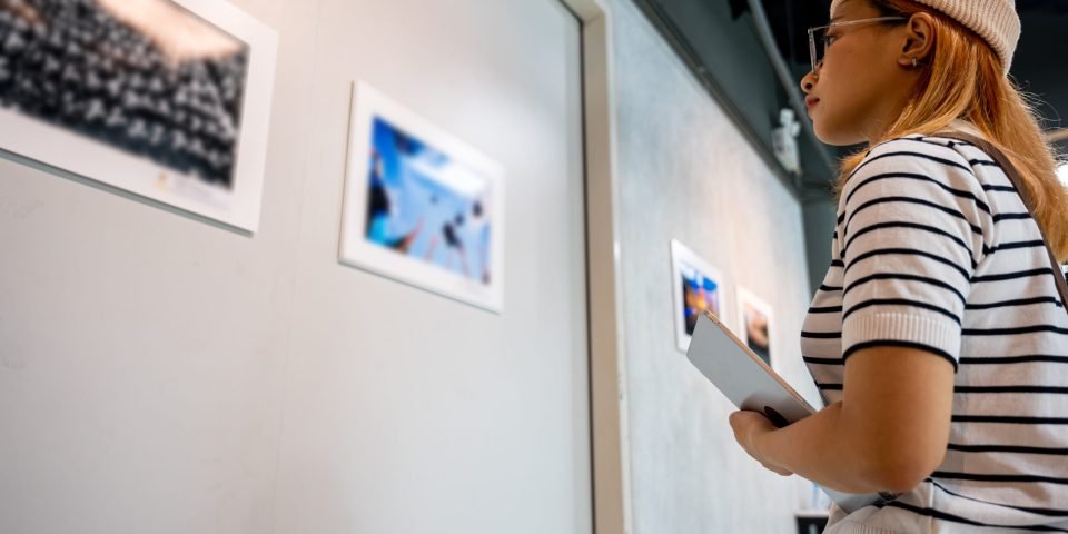 Asian woman holding tablet at art gallery collection in front framed paintings pictures on white wall, Young person at photo frame hold digital book leaning against at show exhibition artwork gallery